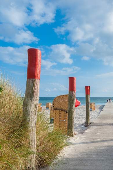 Ein Holzsteg führt zum Meer an einem Strand mit Strandkörben
